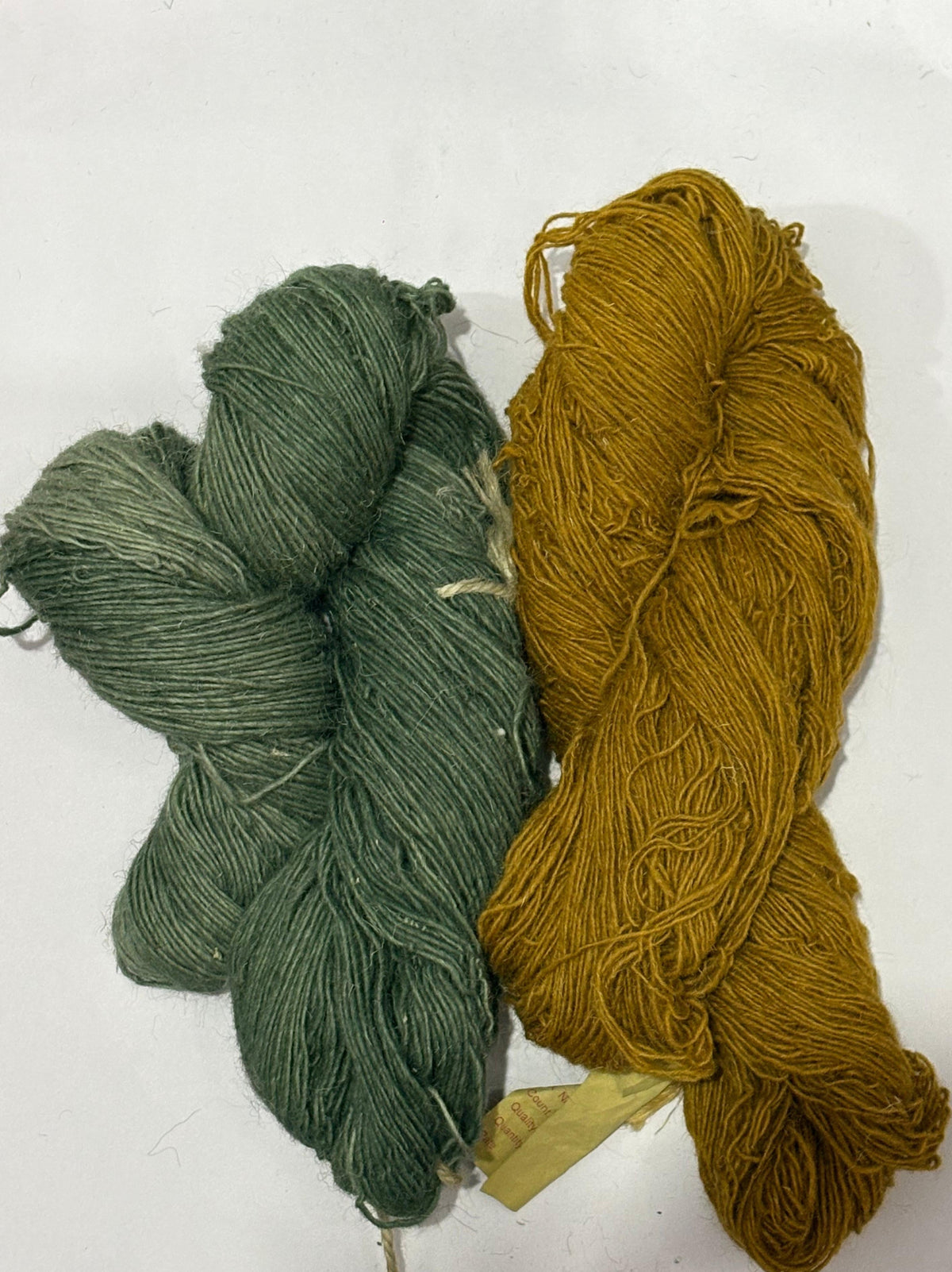 Two skeins of yarn, one in muted sage green and the other in mustard yellow.